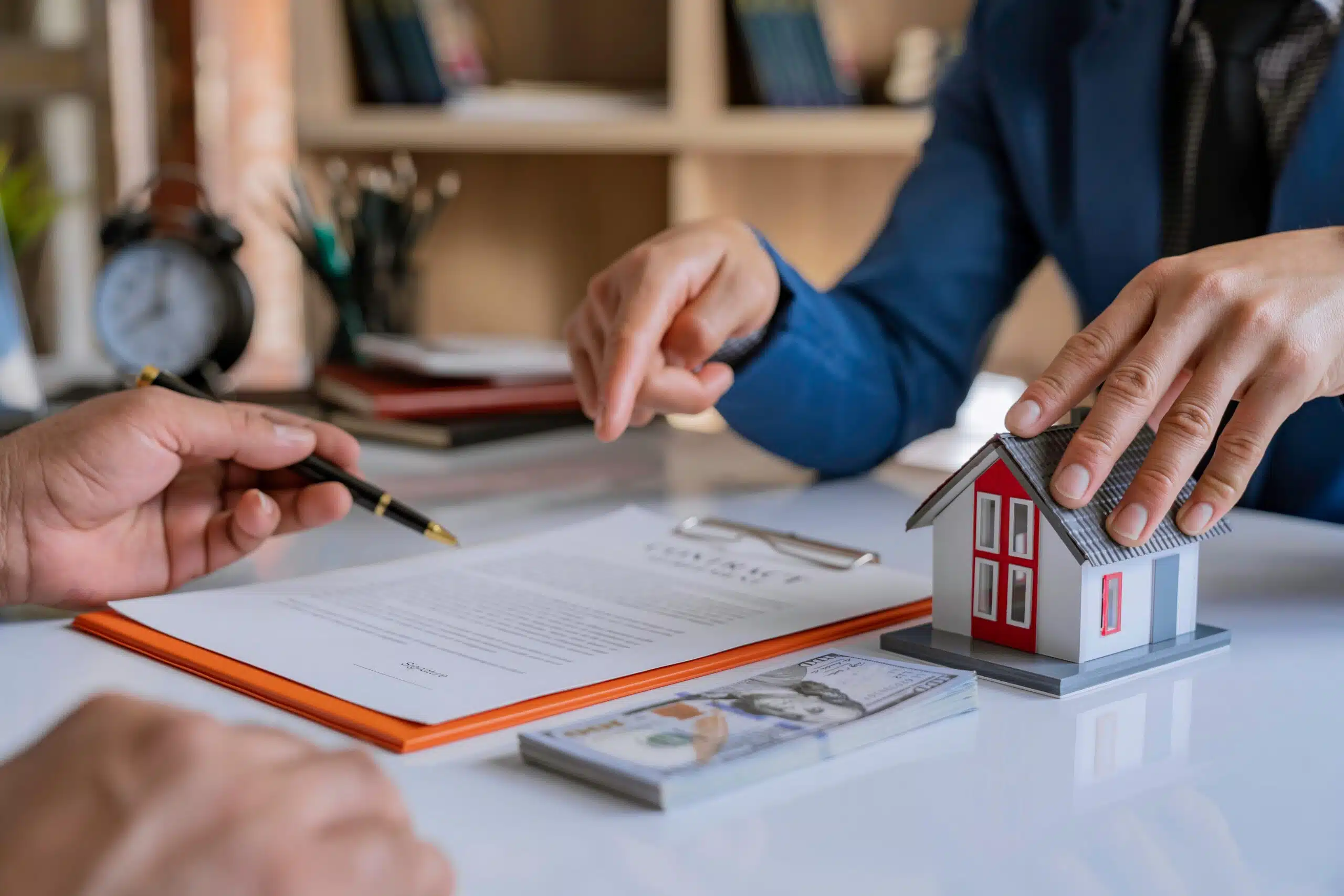 People looking over a mortgage application on a table with a small house figurine. 